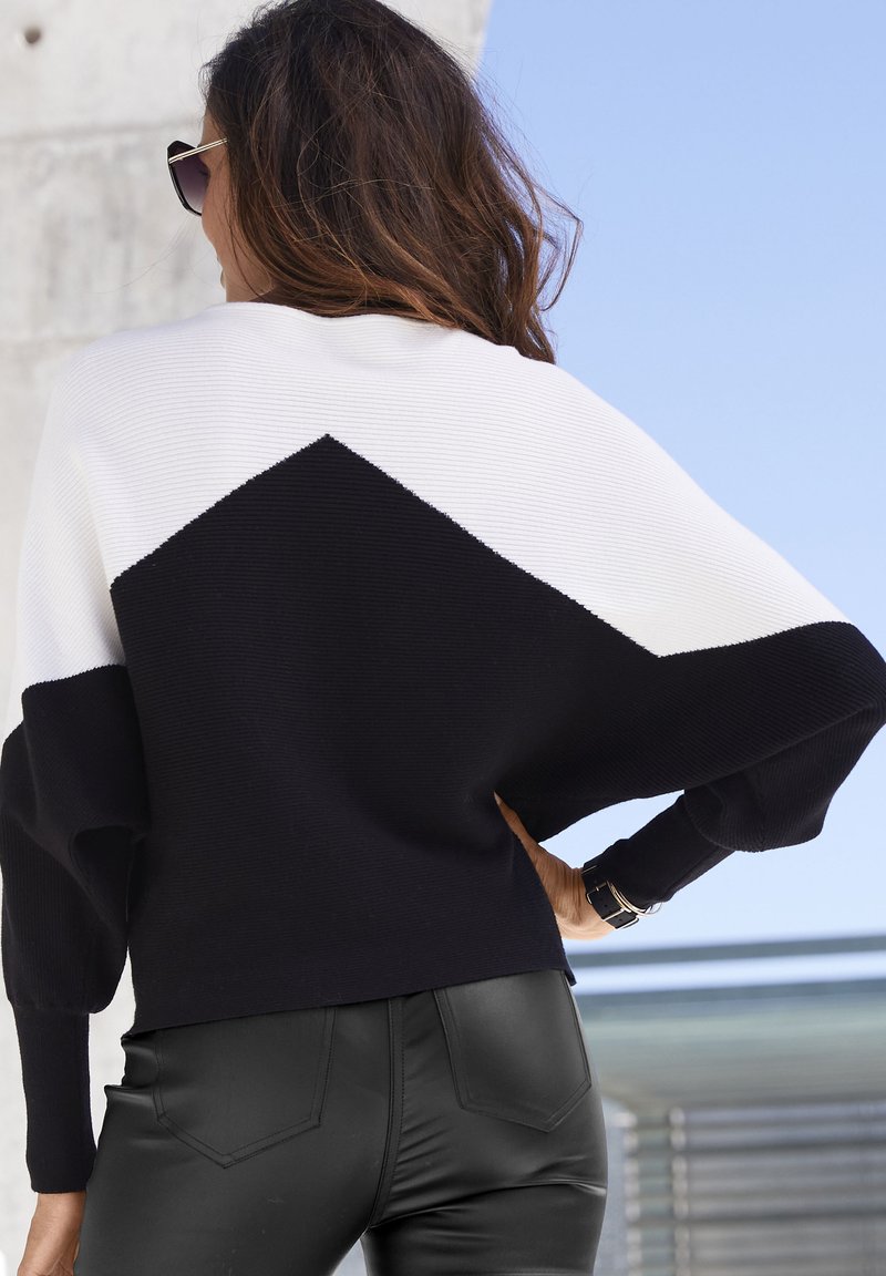 Knit sweater featuring a black, white, and black color block design, with a loose fit and ribbed texture. Paired with black fitted pants.