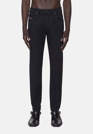 Jeans en denim noir avec une coupe slim, dotés de poches avant, d'un petit logo près de la taille et de coutures renforcées. Portés avec des chaussures noires.