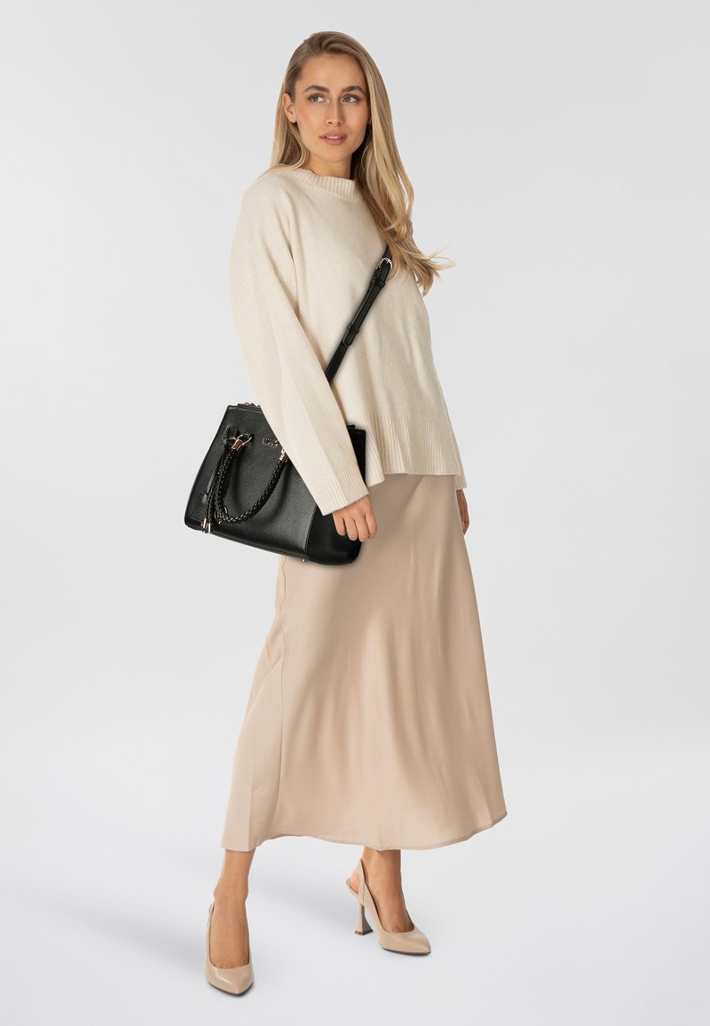 Zwarte leren handtas met kettingdetails, gecombineerd met een beige gebreide trui en een lichtbruine satijnen maxi-rok. Neutrale tinten overheersen.