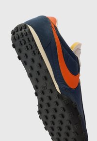 Laufschuhe mit schwarzem Gummistollen und navyblauem Obermaterial, das einen orangefarbenen Nike-Swoosh und eine cremefarbene Mittelsohle aufweist.
