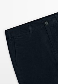 Pantalon en velours côtelé foncé avec une taille dotée de passants de ceinture et d'une fermeture à un bouton. Tissu texturé avec des côtes verticales.