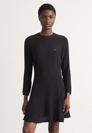 Black long-sleeve dress, A-line silhouette, soft fabric, minimalistic design, featuring small multicolor logo at chest.