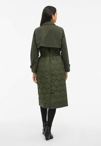 Olivengrønn quiltet frakk med belte i midjen, skulderklaff og knappedetalj nederst, med en glatt ytelse og foret innside.