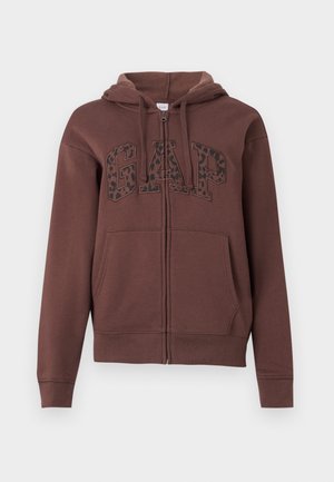 Rjava zip-up kapuca s jakno podlogo, velikimi sprednjimi žepi in napisom "GAP" v črnem leopardjem printu na prsih. Narejena iz mehkega materiala.