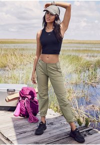 Black cropped tank top, olive green cargo pants with pockets, black sneakers, gray cap, purple backpack, natural outdoor setting.