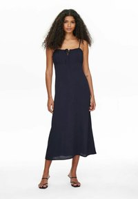 Marineblaues Maxikleid mit Spaghettiträgern, gerafftem Dekolleté und lockerer Silhouette, aus leichtem Stoff gefertigt. Flache Sandalen abgebildet.