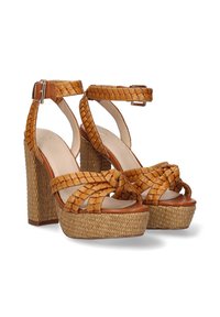 Sandalias de plataforma de cuero trenzado en color marrón con un tacón grueso y un diseño de tiras trenzadas. Cuentan con una correa en el tobillo con una hebilla de metal y una suela texturizada.