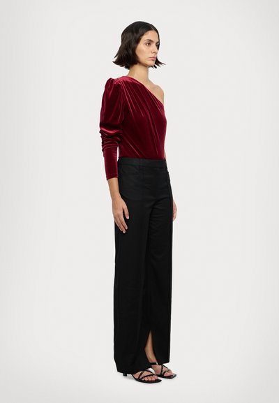Bordeaux Samtoberteil mit einseitigem Design, langen Ärmeln; kombiniert mit hoch taillierten schwarzen Hosen mit Schlitzen an den Knöcheln und schwarzen Riemchensandalen.