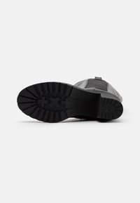 Suela de bota de goma negra con tacos profundos y patrones cruzados, con borde reforzado y diseño lateral liso.