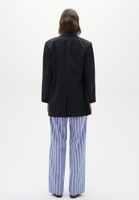Fekete blazer, strukturált dizájnnal, világoskék és fehér csíkos, bőszárú nadrággal párosítva. Sima textúra, minimalista stílus.