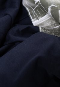 Marineblaue Baumwollstoffe mit strukturierter Oberfläche, versehen mit einem bedruckten Grafikdesign in Grautönen. Der Stoff ist zerknittert und geschichtet.