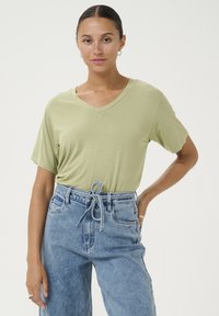 Tricou V cu guler, de culoare verde deschis, fabricat din material moale, cu mâneci scurte, asortat cu blugi din denim de culoare albastru deschis, cu talie înaltă și croială lejeră, detaliu cu șnur.