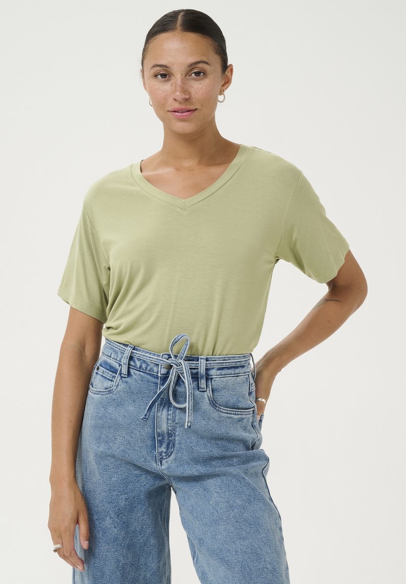 Tricou V cu guler, de culoare verde deschis, fabricat din material moale, cu mâneci scurte, asortat cu blugi din denim de culoare albastru deschis, cu talie înaltă și croială lejeră, detaliu cu șnur.