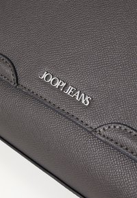 Borsa in pelle grigia con texture, con logo impresso "JOOP! JEANS" e dettagli di cucitura sottile. Forma rettangolare compatta.
