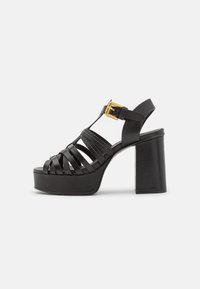 Black platform heels made of synthetic material with a strappy design, block heel, and adjustable buckle featuring a gold accent.