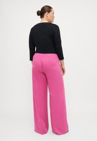 Sort med lange ermer kombinert med høy midje og vide, rosa bukser. Bukserne har elastisk midje og en jevn tekstur.