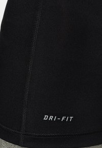 Detailní záběr na černou atletickou látku s viditelným švem a bílým textem "DRI-FIT" vytištěným blízko švu.