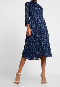 Námořnické květinové šaty s dlouhými rukávy a knoflíkovým zapínáním. Vyrobeny z lehké tkaniny, s plisovanou strukturou a midi délkou.