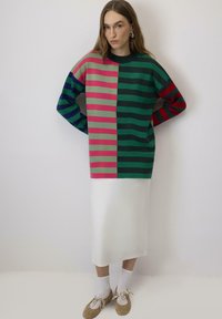 Gestreepte trui in groen, roze en marineblauw; oversized pasvorm met lange mouwen. Witte satijnen rok; gecombineerd met tan schoenen en enkelkousen.