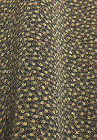 Gros plan sur un tissu foncé avec un petit imprimé floral jaune et une texture fine, montrant des plis doux et des ombres légères.