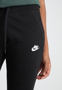 Svarta Nike sweatpants med dragsko i midjan, med vit logobrodyr, sidofickor och ett mjukt, texturerat tyg.