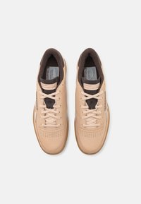 Beige leather sneakers with a textured brown interior, flat laces, perforated toe area, and gum rubber outsole. Features Reebok branding.