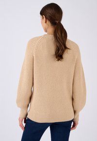 Beige gebreide trui met ribbelstructuur, oversized pasvorm en raglanmouwen. Heeft een ronde halslijn en een iets langere achterkant.