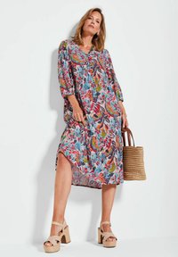 Bloemenprint jurk met een V-hals, driekwart mouwen en een hoge-lage zoom. Gecombineerd met beige platform sandalen en een geweven handtas.