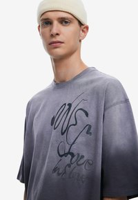 Camiseta de gran tamaño en color púrpura, hecha de algodón, con diseño gráfico de texto en negro. Presenta un cuello redondo y mangas cortas, mostrando una textura deslavada.