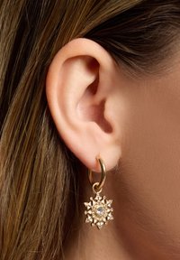 Goldene Creolen mit einem sternförmigen Anhänger, der einen zentralen Strassstein und kleine dreieckige Akzente aufweist. Glatte Metalloberfläche.