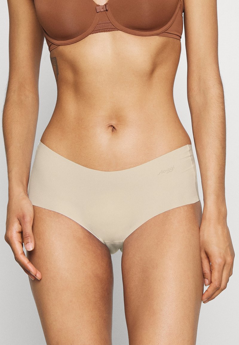 Beige bezešvé spodní prádlo s hladkou, matnou texturou. Navrženo s nízk�ým pasem, minimálním prošíváním a decentním brandingem na pásku.