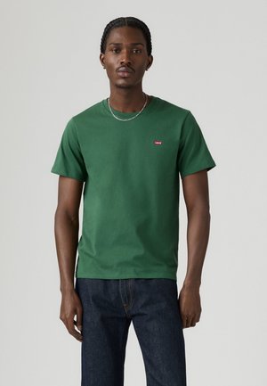Groene katoenen T-shirt met een ronde halslijn en korte mouwen, voorzien van een klein rood Levi's logo op de linkerborst. Gecombineerd met donkerblauwe jeans.