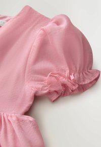 Ružová rukávová balónová manžeta so elastickým zhrnutým manžetom na ľahkej, polopriehľadnej látke z priliehavého odevu.