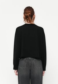 Maglione nero a maniche lunghe con vestibilità relaxed, collo rotondo e spalle scese. Abbinato a jeans dritti scuri a vita alta.