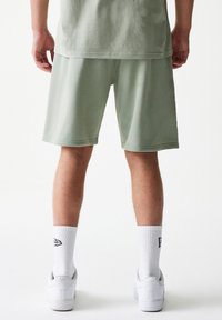 Ανοιχτό πράσινο βαμβακερό σορτς με άνετη εφαρμογή, σε συνδυασμό με λευκές κάλτσες και αθλητικά παπούτσια, που παρουσιάζουν απλό σχέδιο και μαλακή υφή.