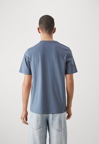 Blå kortärmad t-shirt i bomull med rundad halsringning, mjuk textur och avslappnad passform, som bärs med ljusa denimjeans.