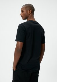 Sort bomulds t-shirt med korte ærmer, rund halsudskæring og afslappet pasform, vist fra ryggen, parret med mørke cargo-bukser.