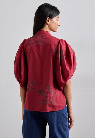 Burgundy floral short-sleeve blouse with puffed shoulders, featuring dark floral prints and a collared neckline. Soft cotton fabric.