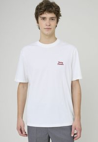 T-shirt en coton blanc avec "Merry Drinker" brodé en rouge, à manches courtes, coupe décontractée, col côtelé et texture lisse.