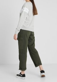 Szara bluza z białym logo na rękawach, zestawiona z oliwkowo-zielonymi spodniami typu cargo z bocznymi kieszeniami, podwiniętymi nogawkami oraz czarnymi trampkami.