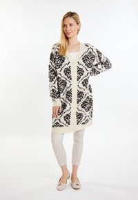 Pletený cardigan v krémové a černé barvě s damaskovým vzorem, se zavinovacím výstřihem, dlouhými rukávy a knoflíky vpředu. Lehká textura.