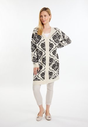 Strickjacke in Creme und Schwarz mit Damaskus-Muster, V-Ausschnitt, langen Ärmeln und Knöpfen auf der Vorderseite. Leichte Textur.