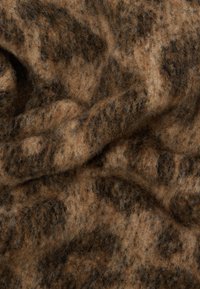 Tissu en laine moucheté marron et beige avec une texture douce et duveteuse, présentant des motifs organiques et un aspect légèrement froissé.