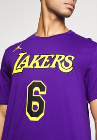 Osoba s fialovým tričkem Lakers, na kterém je žluté a černé číslo 6 na přední straně, ukazující horní část trupu a krk.