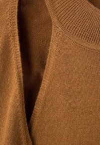 Nahaufnahme von braunem Strickstoff, der eine gefaltete Kante und ein geripptes Kragen-Detail zeigt.