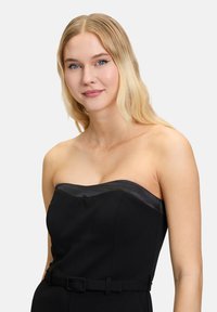 Zwart strappy jurk zonder mouwen met een satijnen rand langs de halslijn, een ceintuurlijn en een getailleerd silhouet. Glad stoftextuur, minimale details.