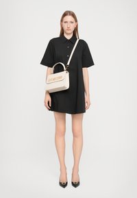 Vestido preto de mangas curtas com colarinho, combinado com uma mala cream com lettering em relevo "LOVE MOSCHINO" e uma alça curta.