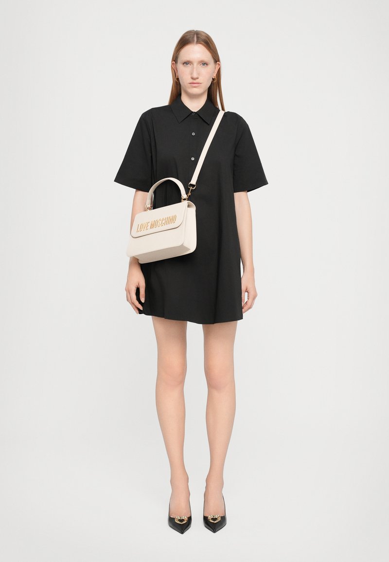 Vestido preto de mangas curtas com colarinho, combinado com uma mala cream com lettering em relevo "LOVE MOSCHINO" e uma alça curta.