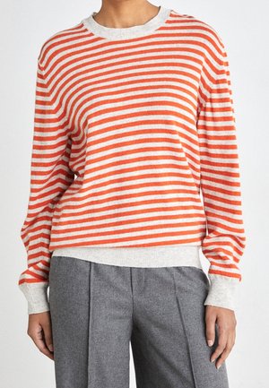Maglione a righe in arancione e crema, con scollo rotondo e maniche lunghe, abbinato a pantaloni grigi plissettati.