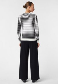 Maglione a righe bianche e nere con collo rotondo, polsini e orlo a costine, abbinato a pantaloni neri larghi. Tessuto liscio, vestibilità casual.